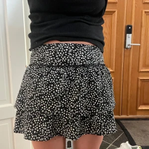 Svart kjol med vita blommor  - Jättefin svart kjol med små vita blommor från zara. Den har shorts inuti vilket gör den otroligt bekväm. Storleken är 152 men som många kjolar så är den töjbar och formar sig väldigt fint. Jag på bilden är 14 år o den sitter perfekt!🥰 Inga defekter!❤️