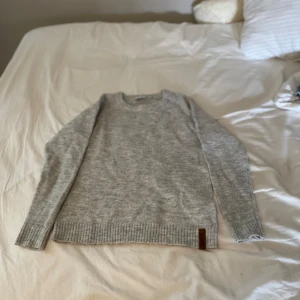 Grå stickad tröja - En grå stickad tröja med långa ärmar och ribbstickade muddar 
