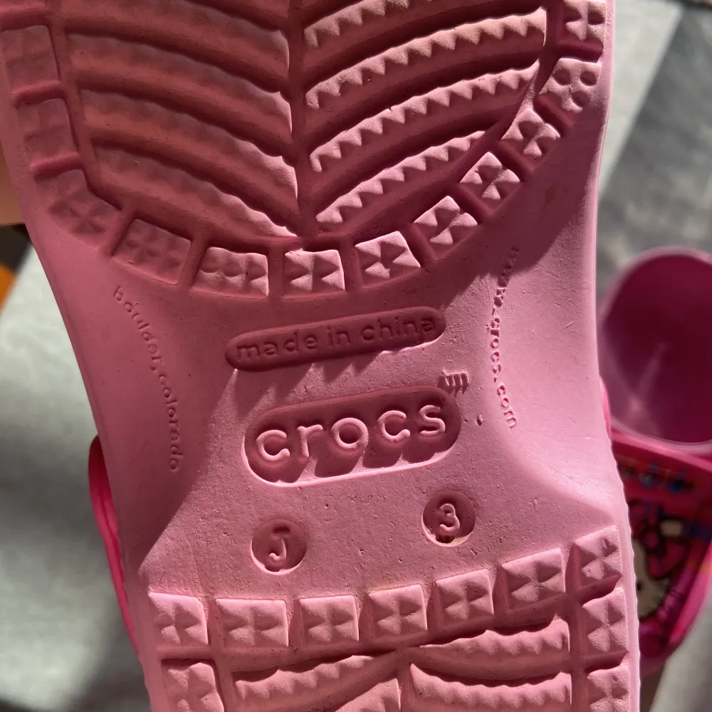 Ett par rosa Crocs med Hello Kitty-motiv. Skorna har en justerbar rem och ventilationshål på sidorna. Hello Kitty-motivet är placerat på ovansidan av skorna och remmen har texten 'Hello Kitty'. de är i strl 3 som motsvarar ungefär 35 kanske 36, super gulliga, lite använda som man kan se på bild 4 annars fina original pris 600kr . Skor.