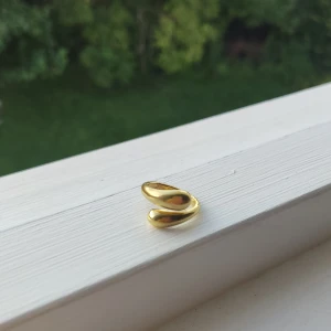 Guldfärgad ring - En elegant guldfärgad ring med en enkel och modern design. Ringen har en öppen form som gör den justerbar i storlek. Helt oanvänd