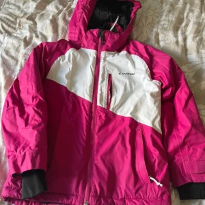 Rosa och vit jacka från Everest - En rosa och vit jacka från Everest med huva och dragkedja. Jackan har långa ärmar och är i välanvänt skick med synliga slitage på vissa ställen.