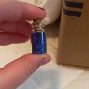 Blå glitterögonskugga i glasflaska - En blå glitterögonskugga i en liten glasflaska med kork. Perfekt för att lägga till en glittrande effekt på ögonlocken.