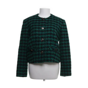 Grön och svart rutig jacka från Sandro - En elegant grön och svart rutig jacka från Sandro Paris. Jackan har långa ärmar och knappar framtill. Den är tillverkad av en blandning av polyester, ull och akryl, med en sekundär tyg av viskos och fickfoder av bomull.