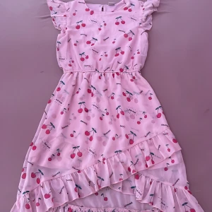 Rosa klänning med körsbär på - Den är rosa med körsbär på och den har volanger. 