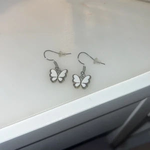 Fjärilsörhängen - Fina fjärilsörhängen. Min kompis gjorde de åt mig men har aldrig använts, därav säljer jag de. Fjärilen är vit med guldkant o själva bågen som fjärilen hänger på är i silver, inget som ser konstigt ut. Kolla profilen för fler smycken mm.💕