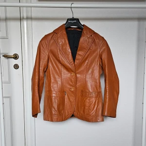 Vintage Läderjacka/Kavaj Janbell 70-tal - Svenskdesignad läderjacka från 70-talet av märket Janbell. Två små svarta fläckar på framsidan vid sidosömmen. Annars väldigt fint skick för sin ålder! Ärm: 39cm, Rygglängd: 60cm, Bystvidd: 90cm, Axlar: 39cm, Midja: 43cm