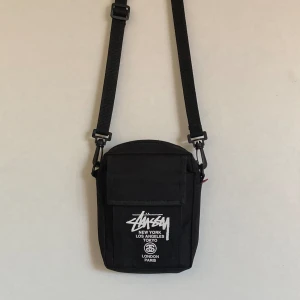Stussy väska - Snygg liten väska ifrån stussy, justerbar rem och passar perfekt som en crossbodybag. Väldigt bra skick och inte något man ser så ofta. Kom med bud och ställ gärna frågor!