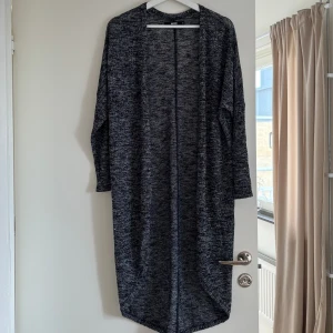 Lång kofta  - Låång mysig kofta i grå/svart mönster. Slutar ca 2dm från golvet och jag är 165cm lång. Lite nopprig på vissa ställen därav billigare pris.
