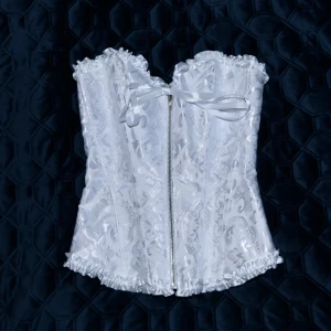 Vit korsett - Vit korsett med dragkedja fram och korsettsnörning i ryggen för bästa passform. Har 12 formstavar i hårdplast som framhäver en fin timglasfigur. Korsetten ger ett fint stöd, passform och hållning.  Aldrig använd då den är för stor vid bysten.
