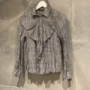 Volangblus Zara - Hundtands/rutig grå volangblus från Zara. Fint mönster, med detaljer av guldtråd.  Mjuk och skön kvalitet. Sparsamt använd, hittar inget att anmärka på.