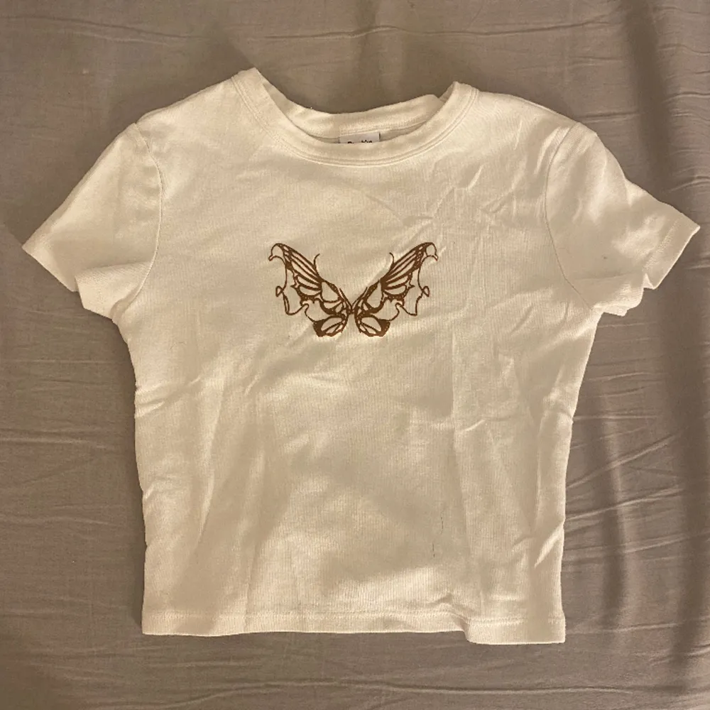 Säljer denna jättegulliga croppade t-shirten från bershka med ett brunt fjärils märke. Används rätt så mycket men är i bra skick ändå. För fler bilder/mått osv kom privat!. Toppar.