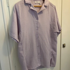 Weekday- kortärmad skjorta  - Kortärmad skjorta i färgen ljuslila. Axelbredd  43 cm, längd 82 cm. Material: polyester och viskos. Endast använd ett par gånger. I fint skick!