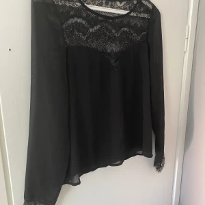 Spetsblus - Nyskick. Svart top med spetsdetaljer. Stl M