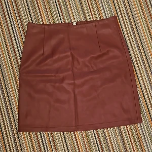 Läder kjol - En snygg läder kjol i vinröd färg. Har en dragkedja där back.