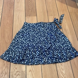 Mörklblå kjol - En kort kjol i storlek S med en rosett som kan knytas vid sidan. 