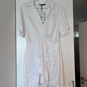Vit klännkng - Vit kortarmad klänning från zara. Helt ny med prislapp kvar. Lite blankt tyg och snygg ”Knut” i mitten längst fram i midjan som markerar lite. 