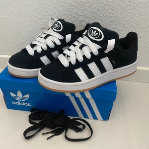 NYA Adidas CAMPUS00s - Adidas Originals Campus 00 s j Storlek: 37 1/3 Färg: Svarta (Core Black / Cloud White / Cloud White) Ingår både vita och svarta skosnören.  Nya och oanvända. Ligger kvar i kartong.  Äkta och köpta i Sverige. Sista paret. 