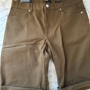 Brun/gröna jeansshorts från HM  - Ett par brun/gröna jeansshorts som funkar perfekt för sommaren. Byxorna är från HM och är i passformen slim fit. Shortsen är tunga men mjuka och lätta att röra sig i. 