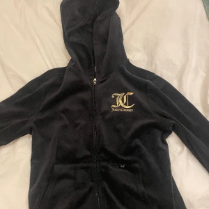 Juicy tröja svart med guldbolstäver  - En svart juicy tröja med guldig text både bak och fram. Tyvärr har den fått en liten lite vit färgfläck på framsidan av tröjan. Kan vara så att fläcken kan tvättas bort men vet ej (syns på bilden). Köpt på kidbrandstore för ca 800kr. Använd.