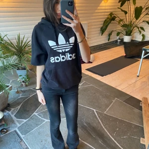 Adidas kortärmad hoodie - En supercoola adidas hoodie med korta ärmar i strl M med ett stort adidas tryck på framsidan (obs att ärmarna är avklippta från långa ärmar)🌹 hoodien är något solblekt vilket jag tycker endast är ett plus! Annars har den inga synliga defekter💋