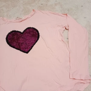 Ljusrosa tröja med glittrigt hjärta som man kan ändra färg på - Säljer nu denna coola ljusrosa tröja som har ett rosa paljetthjärta på och drar man paljetterna åt andra hållet vlir det ett silvrigt brustet hjärta. Knappt använd så skicket är bra. Storlek 146-152 men passar mig som brukar ha xs eller s också!