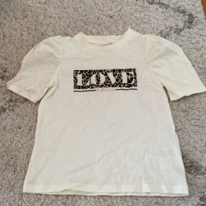 Vit fin t-shirt med en love logga på med puffiga axlar🤍 - Jag säljer en vit t-shirt med en love logga på med puffiga axlar. Tröjan är i storlek 128och är ifrån Lindex 🤍