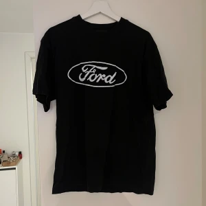 Svart t-shirt med Ford-logga - En svart t-shirt med Ford-logga i vitt på bröstet. T-shirten har korta ärmar och en rund halsringning.