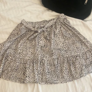 Vit kjol med svarta prickar - En vit kjol med svarta prickar och volangdetaljer. Kjolen har en knytning i midjan. Har inte kvar någon lapp så vet inte märket eller passform men tror ungefär xs💋💓😻