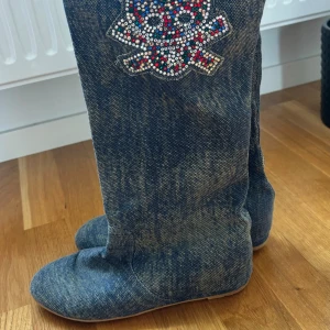 Höga stövlar med döskalle - Jättesnygga stövlar i denim med döskalle tryck! Finns få slitningar där bak som syns i sista bilden