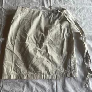 Beige kjol från Camel Collection - En beige kjol från Camel Collection i storlek 38. Kjolen är tillverkad av 100% bomull och har en enkel design med ett knytband i midjan.