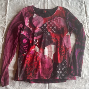 Mönstrad långärmad tröja från Soleil Rouge - En färgglad och mönstrad långärmad tröja från Soleil Rouge. Tröjan har en mix av röda, rosa och lila nyanser med abstrakta mönster. Den har en rund halsringning och är tillverkad i ett mjukt och bekvämt material.