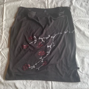 Svart kjol från Connect - En svart topp från Connect med ett blommigt mönster i rött och vitt. toppen har en enkel design utan synliga detaljer som dragkedjor eller knappar.