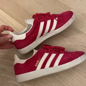 Röda adidas gazelle - Röda adidas gazelle. De är lite rosa i tiden som man kan se på bild 2 samt har en gul rand inuti men den syns inte vid användning. Bortsätt från det är det inga synliga skavanker och skorna ser inte flitigt använda ut. (Skriv för fler bilder)