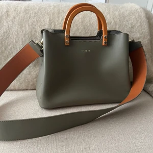 Fin grön väska med bruna detaljer - Jättesöt väska med både ett långt avtagbart band och kortare handtag!! Köpt second hand, frakt tillkommer