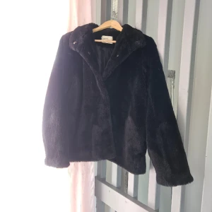Svart mjuk fuskpäls - Riktigt mjuk fuskpäls, håller en lagom varm även på vintern. Som ny! Storlek L B 56. L 72.