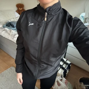 Svart träningsjacka från puma - Svart träningsjacka från puma, ganska tunn men fungerar vid vind. Har använts men fortfarande i bra skick!