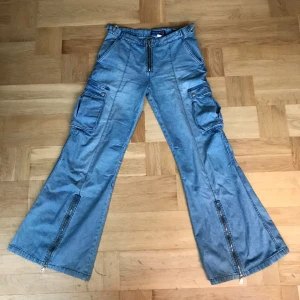 Jeans med fickor - Unika Lågmidjade utsvängda jeans med drag kedjor, fickor och massa andra detaljer 🌻 Midjemått rakt över = 40 cm Innerbenslängd = 81 cm Längden på hela byxorna = 104 cm