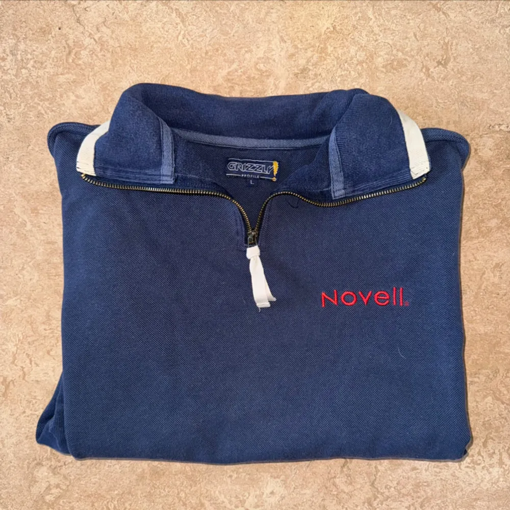 Fin half zip tröja från märket grizzly med broderad text ”novell” i färgen mörkblå. Liten fläck vid sidan, skickar bild vid intresse. Hoodies.