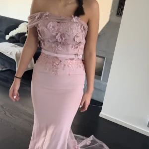 Rosa balklänning  - Fin rosa lång festklänning som varit använd 1 gång. Den är fin i material och genomskinlig där bak som ni ser på bild. Om man vill ta bort ärm delen så kan man göra det också. Den har även små blommor på som matchar till släpet. Pris kan diskuteras 