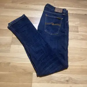 Snygga Nudie jeans i en mörkblå färg! Modellen på jeansen är tight long john, alltså slim fit. Bra skick förutom en lagning vid skrevet som varken märks eller syns vid användning!