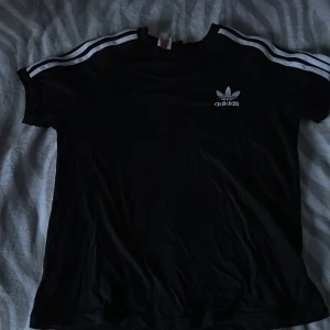 Adidas t-shirt - Svart t-shirt med vita ränder. Väldigt fin och i mycket bra skick. Passar flera storlekar beroende på hur du vill att den ska sitta💞