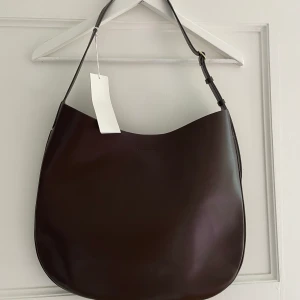 Väska läder ARKET - Rundad axelremsväska ARKET kromfritt läder. Magnetisk stängning och reglerbar axelrem med ett rund spänne. Innerficka Bredd: 40 cm. Höjd: 36,5 cm 100% läder Oanvänd  Lapp och skyddande plast kvar Ord pris 2290kr https://www.arket.com/sv_se/women/bags