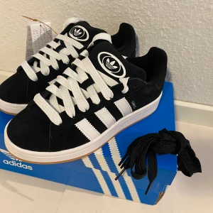 Nya svarta Adidas Campus 00s -storlek 38 2/3 - Adidas Originals Campus 00 s j Storlek: 38 2/3 Färg: Svart (Core Black / Cloud White / Cloud White) Ingår även svarta skosnören.  Nya och oanvända. Ligger kvar i kartong.  Kommer EJ från någon massbeställning utomlands. Garanterat äkta. 