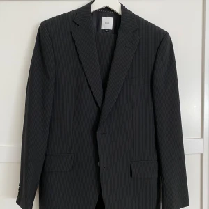 Snygg kritstrecksrandig svart kostym - Bläck kritstrecksrandig svart kostym, mycket bra skick. Storlek 46 eller small. Knäppning 2 knappar, 6 fickor  Pris 450kr Nypris 1990kr