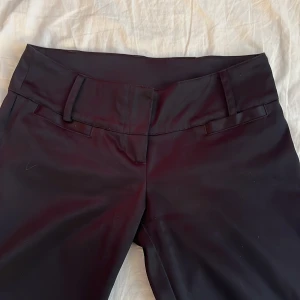 Lågmidjade kostymbyxor  - Lågmidjade kostymbyxor utsvängda vid benen i ett glansigt material.