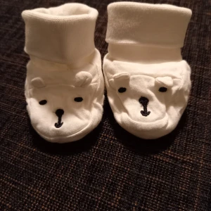 Tossor strl. 50/56 - Vita tossor med björnansikte till nyfödd i storlek 50/56 från Lindex. Små påsydda öron och vikbar mudd. I fint skick, inga hål eller fläckar. Unisex  Tvättade i parfymfritt tvättmedel och utan sköljmedel. 