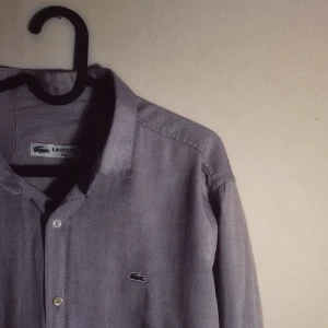 Skjorta  - Skjorta köpt från Lacoste. Fint skick använd endast ett fåtal gånger. Fläckfri. Är i Storlek XXL men passar XL. Fin violett färg och skönt material. Extraknapp medföljer. 