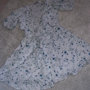 överlappande klänning - vit överlappande klänning med blåa blommor på i linne. Strl xs, man tar på sig den som en ”rock” och knyter den runt midjan. Har bara använts 1 gång, säljer för den är för kort för mig som är 167 cm lång. Kom privat för fler bilder eller frågor💕