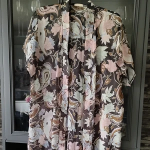 Lång kaftan - Lång kaftan med vårigt mönster i tunnt tyg. Botten är svart/mörkbrun. Aldrig använd.