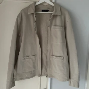 Overshirt  - Snygg overshirt/ziptröja säljes. Färgen är ljusgrå/beige, Storlek är M och tröjan är i nyskick. Köptes för 999kr på Brothers för några månader sedan, säljes för 350kr.